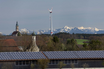 Solaranlage auf einem Dach, dahinter ein Windrad und das Alpenpanorama