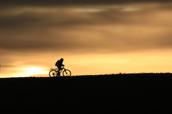 Radfahrer auf einem Hügel, dahinter ein Sonnenuntergang